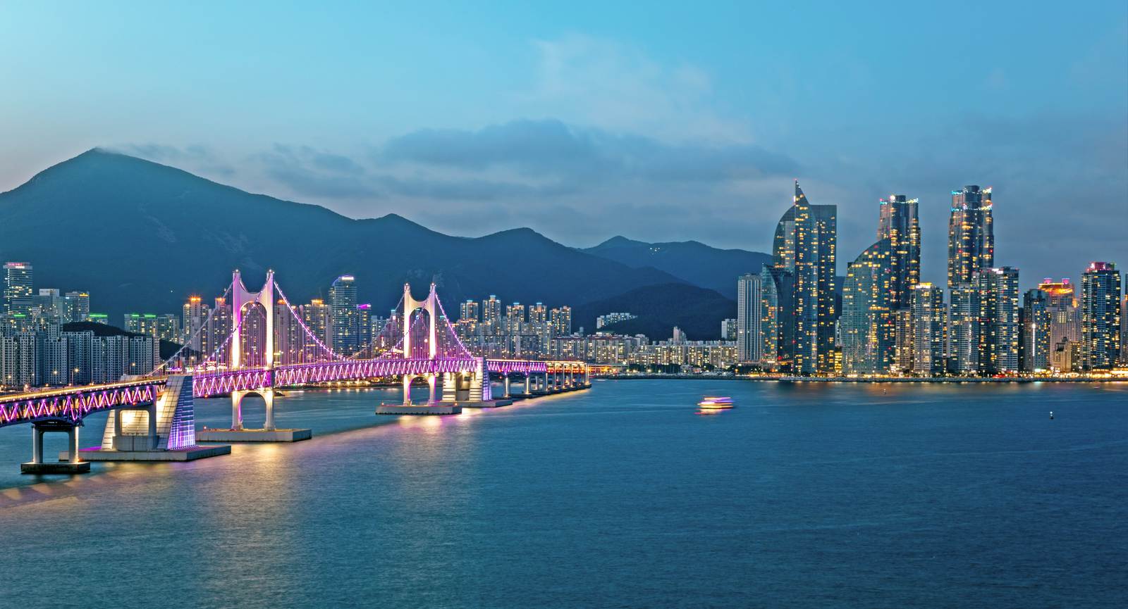 黄昏时分的广安大桥亮起紫色灯光，背后是海云台的摩天楼与群山